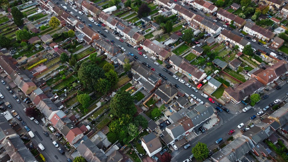 An aerial view of a residential area along Mapesbury Road in Cricklewood, showing a row of terraced houses with pitched roofs, some covered in light snow. The road in the center is lined with parked c